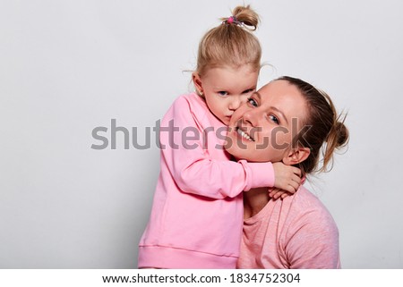 Little daughter hugging and kissing her mother spending time together in pink clothes over gray background. Mother's Day love family, parenthood childhood concept