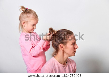 4-5 year old little daughter does the hair of a her mother. Love family spending time together in pink clothes