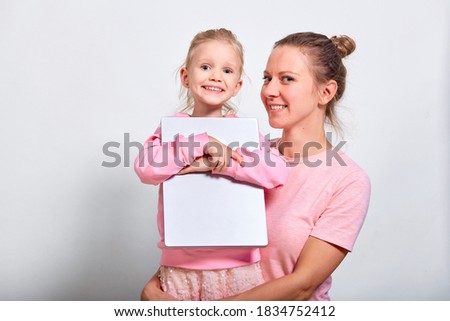 Virus protection concept. Closeup portrait of ?ute girl 4-5 year old and her mother in pink clothes, showing laptop which medical mask on screen, gray background