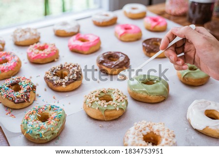 close up of hands decorating various donuts with chocolate frosted, pink glazed and donut sprinkles on the table Royalty-Free Stock Photo #1834753951