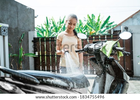 asian young girl washing his motorcycle scooter with water at home