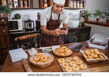 male chef smiles while taking pictures of donuts using a smartphone for online marketing of homemade products