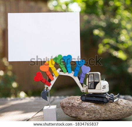 model of toy excavator on  large stone. Attached to excavator's boom are bright pins and blank sheet of paper for text. place for announcement, business - congratulations for construction company