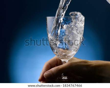 Water pouring into glass. Female hand, holds the stem..