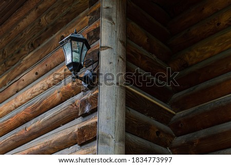 Old black street glass lamp hangs on corner of wooden house made from round orange brown logs. Russia