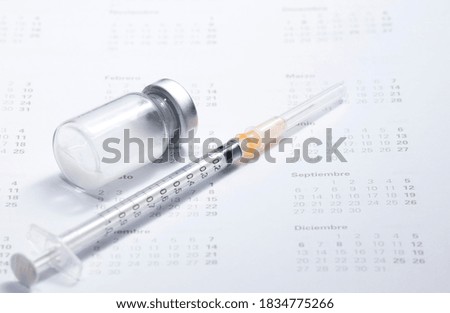 Medical concept. In the 2021 calendar, (names of months in Spanish, February, March, April, September, December,) syringe with container of epidemic vaccine.
