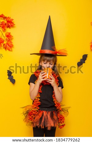 Beautiful little girl dressed as a witch for Halloween, drinking cup of hot tea, isolated on yellow colored background
