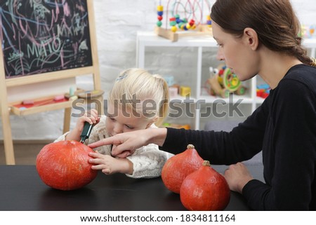 Cute little girl preparing Halloween decorations with her mother. Autumn DIY craft at home.	