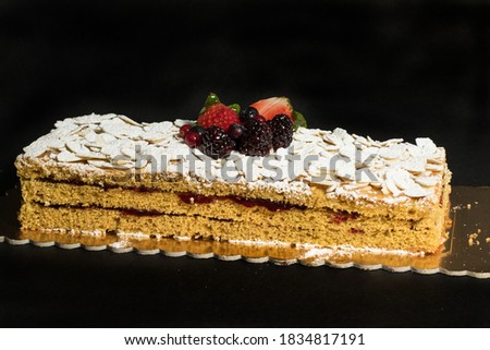 
three-layer cake filled with cream and berries, topped with a carpet of almonds covered with icing sugar, with a decoration in the center of strawberries and berries