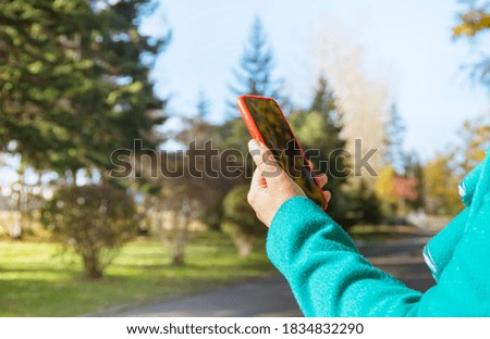 Close up photo of female hands with smartphone. Autumn trees on background