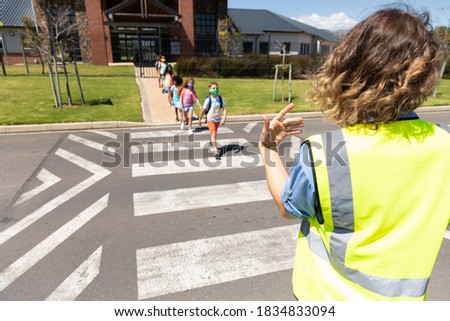Multi ethnic group of school children wearing face masks, crossing the street with Caucasian policewoman saying its safe. Education back to school health safety during Covid19 Coronavirus pandemic. Royalty-Free Stock Photo #1834833094