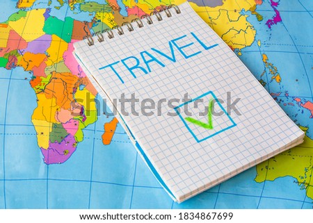 Check mark in box` "Travel" in notepad against colorful world map background. Post-pandemic travel concept. Allowed to travel