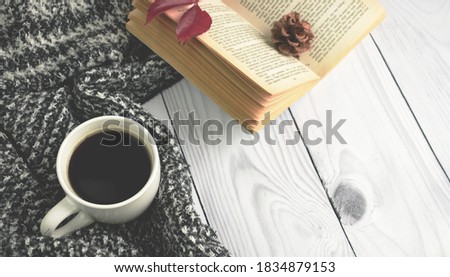 A cup of black coffee with book, flower and red autumn leaf with warm woolen clothes on the brown background. Flat lay, top view, copy space. Autumn cozy composition, fall concept.