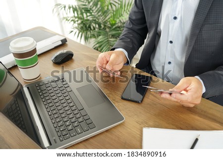 a male businessman chooses a credit card to make an online purchase using a laptop and smartphone
