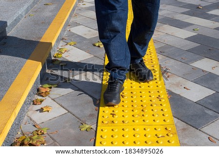 Man walking on yellow blocks of tactile paving for blind handicap. Braille blocks, tactile tiles for the visually impaired, Textured ground surface indicators located on sidewalks, stairs.