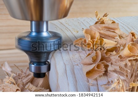 Woodworking shank router bit. Shaping copy milling cutter with ball bearing. Rotating cutting tool clamped in chuck of working machine detail when forming wood plank edge. Wooden curled shavings pile. Royalty-Free Stock Photo #1834942114