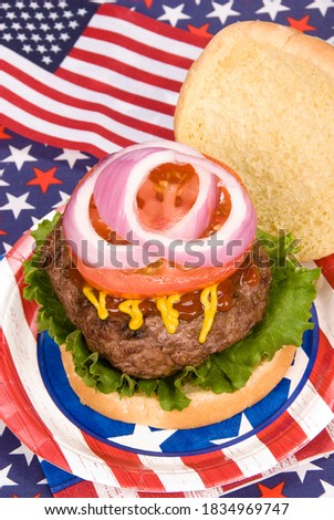 A juicy hamburger with tomoato, onion, mustard and ketchup with a fourth of July patriotic theme