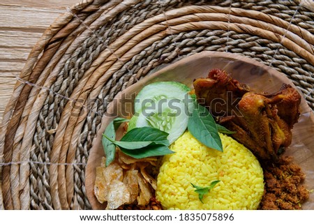 Yellow Rice with traditional fried chicken cucumber coconut stir fried called serundeng and beef abon on a wood plate and brown textured wood table
