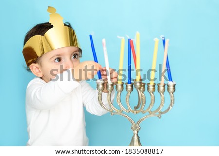 Kid celebrating Hanukkah Israel holiday. Little jewish boy puts candles on traditional menorah.
