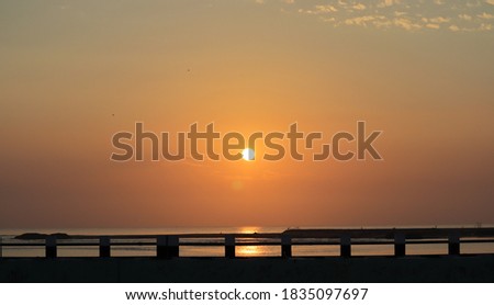 Beautiful landscape photography background with golden natural rays of the sun in the sky after sunrise from the ocean across the silhouette bridge