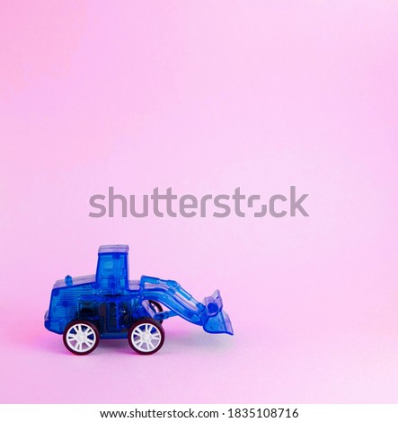 Colorful toy blue plastic tractor isolated on pink background. Blue excavator. Toy for children.
  Side view. Copyspace for text. Poster for advertising.