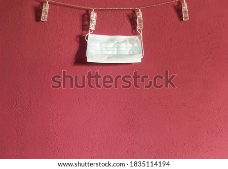 Used medical mask drying on a string hanged on a red / magenta wall. Clipped to a clothesline with plastic laundry clips.  Royalty-Free Stock Photo #1835114194