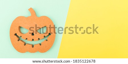 Halloween background idea.Flat lay wooden Jack o lantern spooky pumpkin on green yellow paper color background.Halloween design with copy space for text advertising.Background idea in Autumn October.