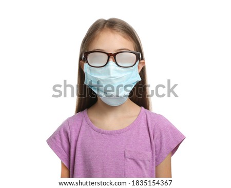 Little girl with foggy glasses caused by wearing disposable mask on white background. Protective measure during coronavirus pandemic