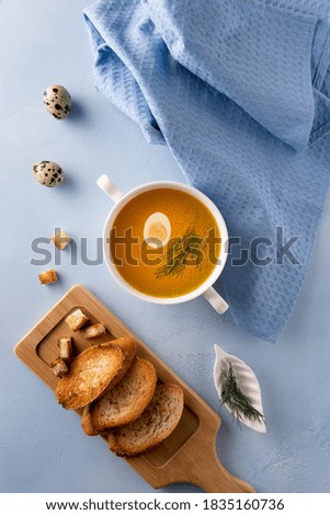 White soup bowl with bouillon, quail egg and fennel leaf on blue background. Linen textile, whole eggs and toasted bread. Flat lay. Vertical orientation. Homemade healthy eating and dieting concept.