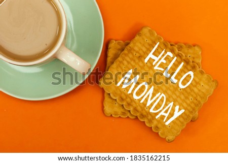 milk coffee cup with hello monday concept on biscuit isolated on orange background