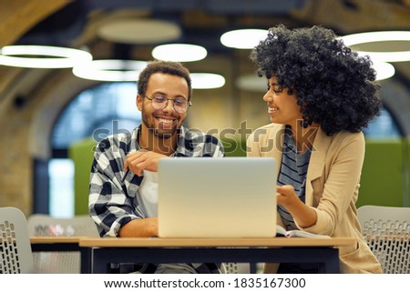 Two young happy multiracial business people sitting at the desk in the modern office, using laptop and discussing project, man and woman working together in coworking space Royalty-Free Stock Photo #1835167300