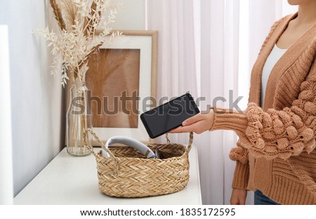 Woman putting smartphone into wicker basket with gadgets at home. Digital detox concept Royalty-Free Stock Photo #1835172595
