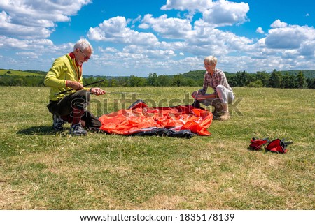 Senior man and woman having fun together while putting up a tent in nature with beautiful clouds in the background