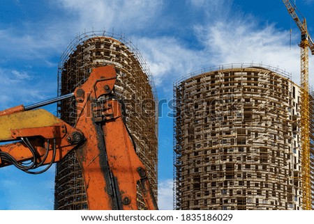 Part of a construction machine (excavator or crane) with multi-storey building under construction with scaffolding (new residential complex) on the background, Moscow, Russia