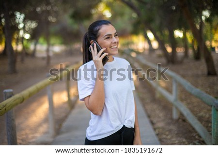 Young beautiful woman wearing sport clothes in the forest very happy and smiling, talking on the phone