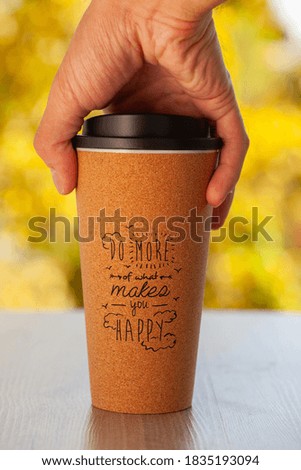 reusable eco-friendly craft coffee Cup for takeaway in a man's hand on a background of Golden foliage. Eco glass on the table in a cafe