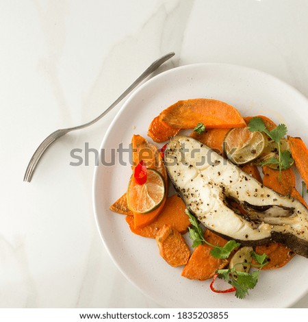 flat lay plate of baked halibut steak with sweet potato, lime, chili and rosemary on light marble table, space for text
