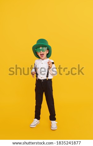 Smiling little child boy in green leprechaun hat on yellow background. St. Patrick Day celebration. Funny face