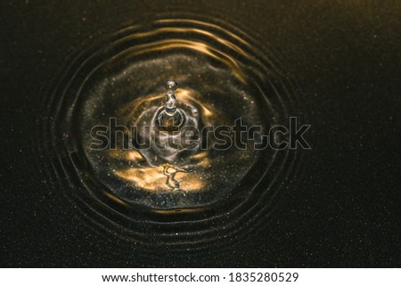 Macro photo of water drops falling into a pool of water, causing a splash. High speed flash photography technique used to freeze the action. 