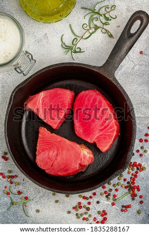 Raw Tuna fish steaks with sea salt, pink, green and black pepper and rosemary for grill or cooking in a cast iron pan. Prepare a delicious dinner. Selective focus and copy space