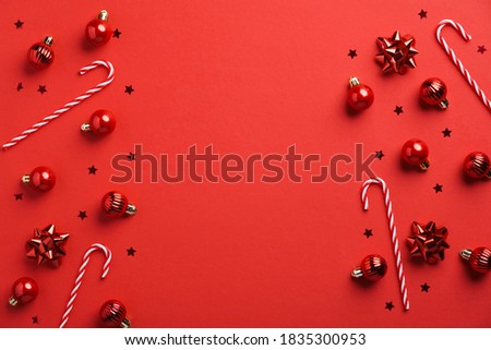 Christmas frame border made of baubles, decorations, candy canes, confetti on red background. Flat lay, top view. Xmas banner mockup with copy space.