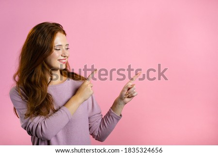 Happy smiling woman presenting and showing something isolated on pink background. Portrait of girl, she pointing with arms on her left with copy space.
