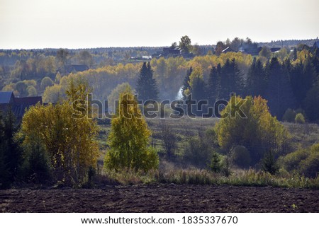 A small village among fields and colorful autumn forest. Autumn is in full swing in the foothills of the Western Urals.