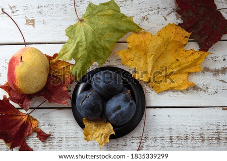 Pear, plum and maple leaves on white wooden background