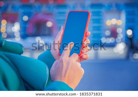 Closeup photo of female hands holding modern smartphone with blank screen. Mockup ready for text message or content. Woman's hands with cellphone. Empty display. Night street, bokeh light 
