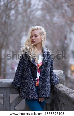 Blonde girl with curly hair and closed eyes, posing in profile, stand on balcony, cold outside.