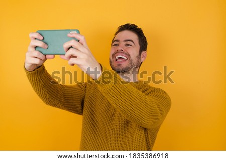 Young man wearing casual sweater and over isolated yellow background taking a selfie to post it on social media or having a video call with friends.