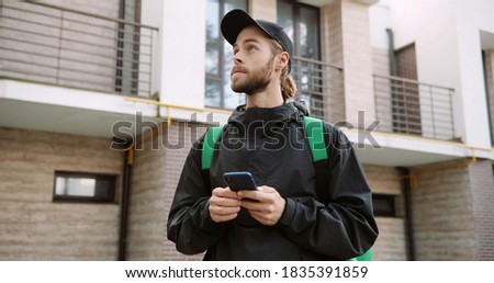 Food delivery courier with backpack using navigation on phone to find address.