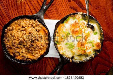 Steakhouse side dishes. Asparagus, salad, tomatoes, mashed potatoes, red onions, cream cauliflower, pickled peppers, seasoned meats served in cast iron skillet. Traditional appetizer items.