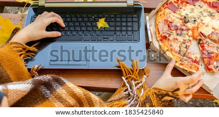 hands on computer keyboard with fallen leaves and pizza on a blanket. outdoor work and fast food